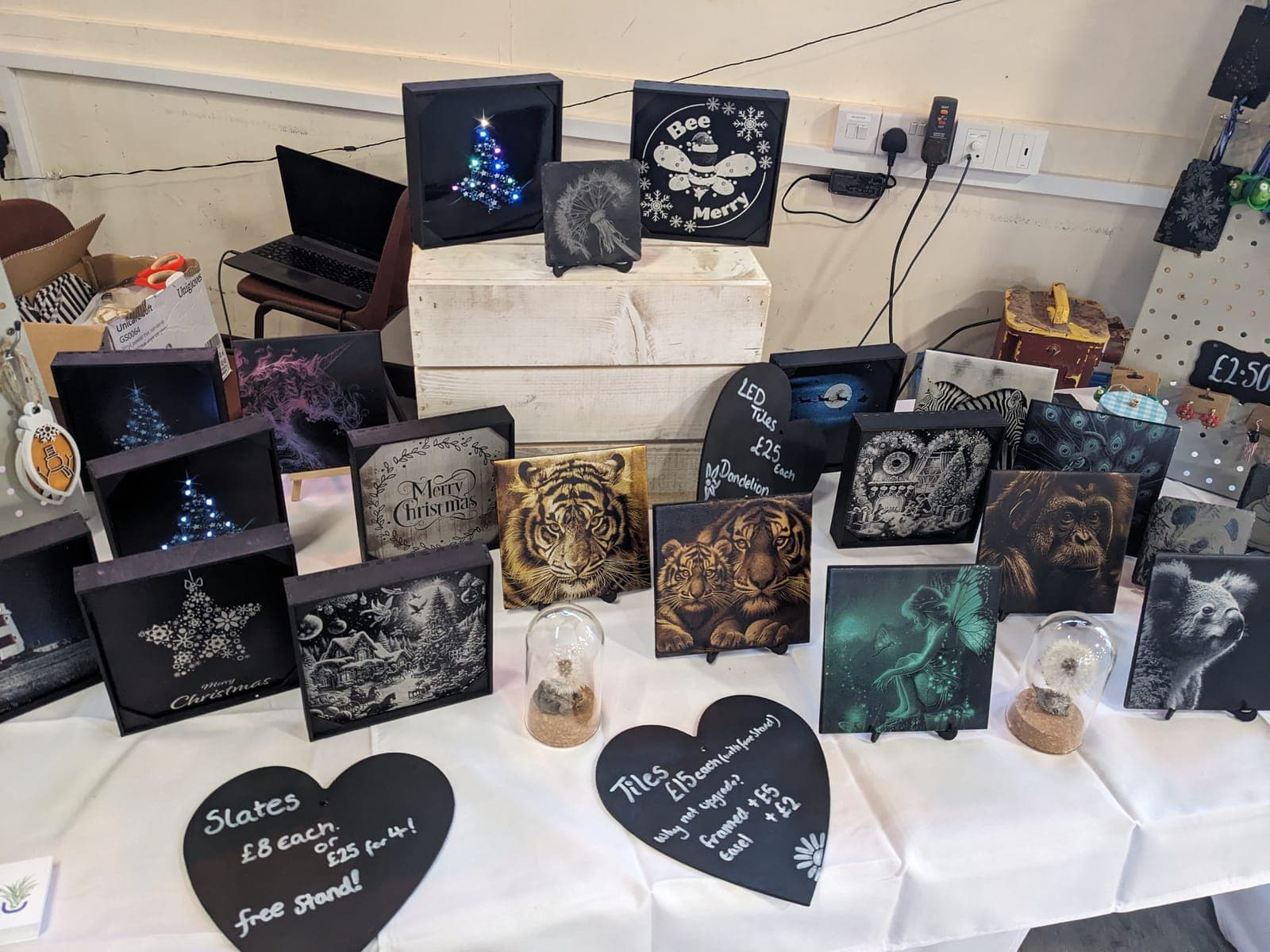 A craft fair table covered in engraved slates and tiles, with chalkboard price hearts