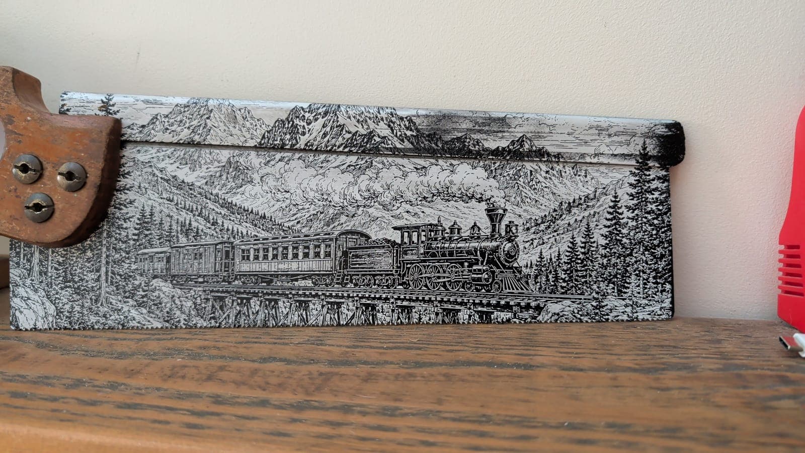 A steam train crossing a mountain valley, engraved along an old hand saw