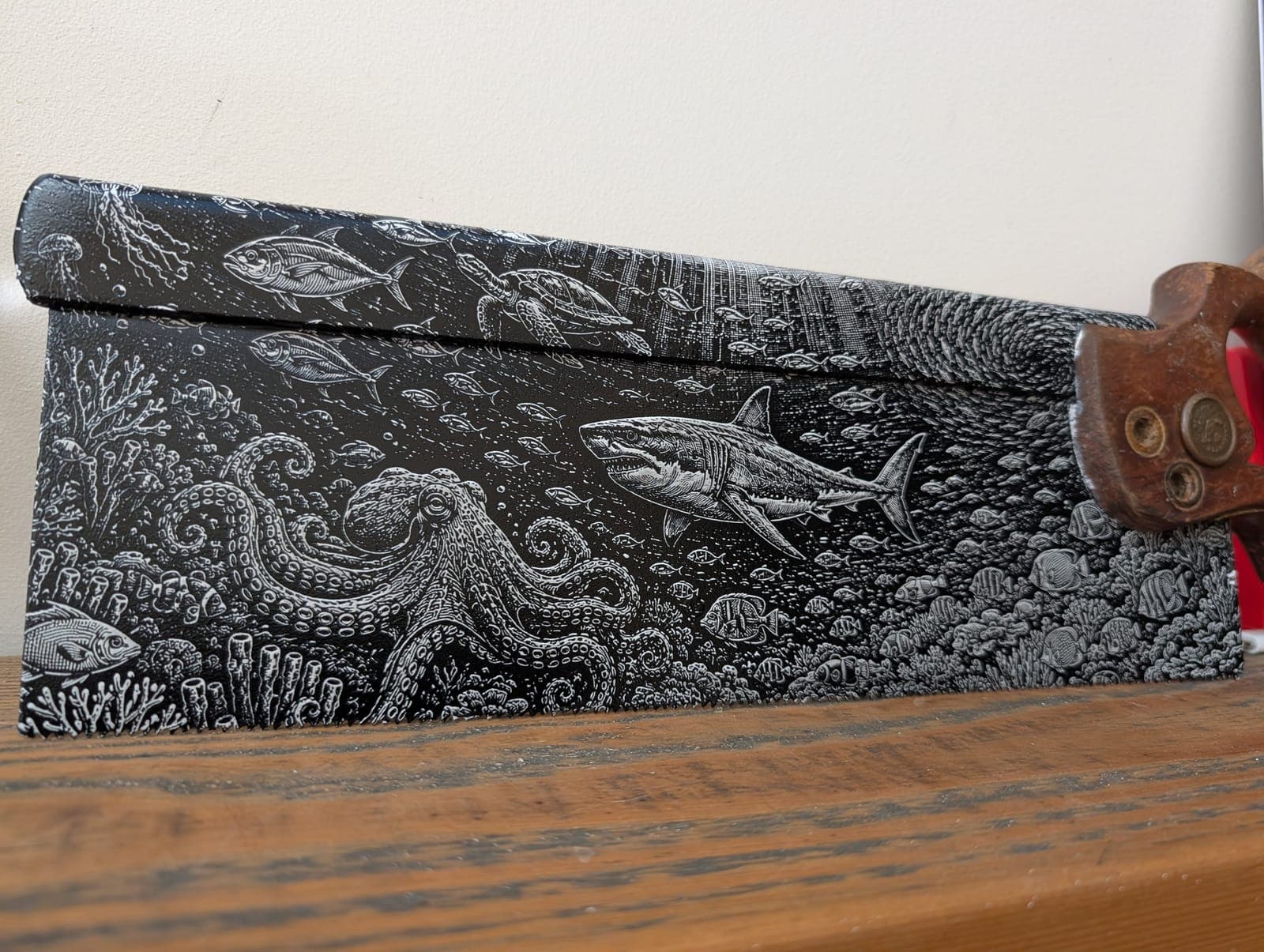 An octopus, shark and fish among coral, engraved along an old hand saw