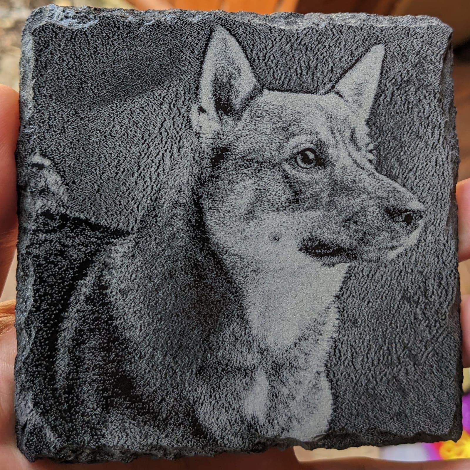 A detailed portrait of a dog engraved on a slate coaster