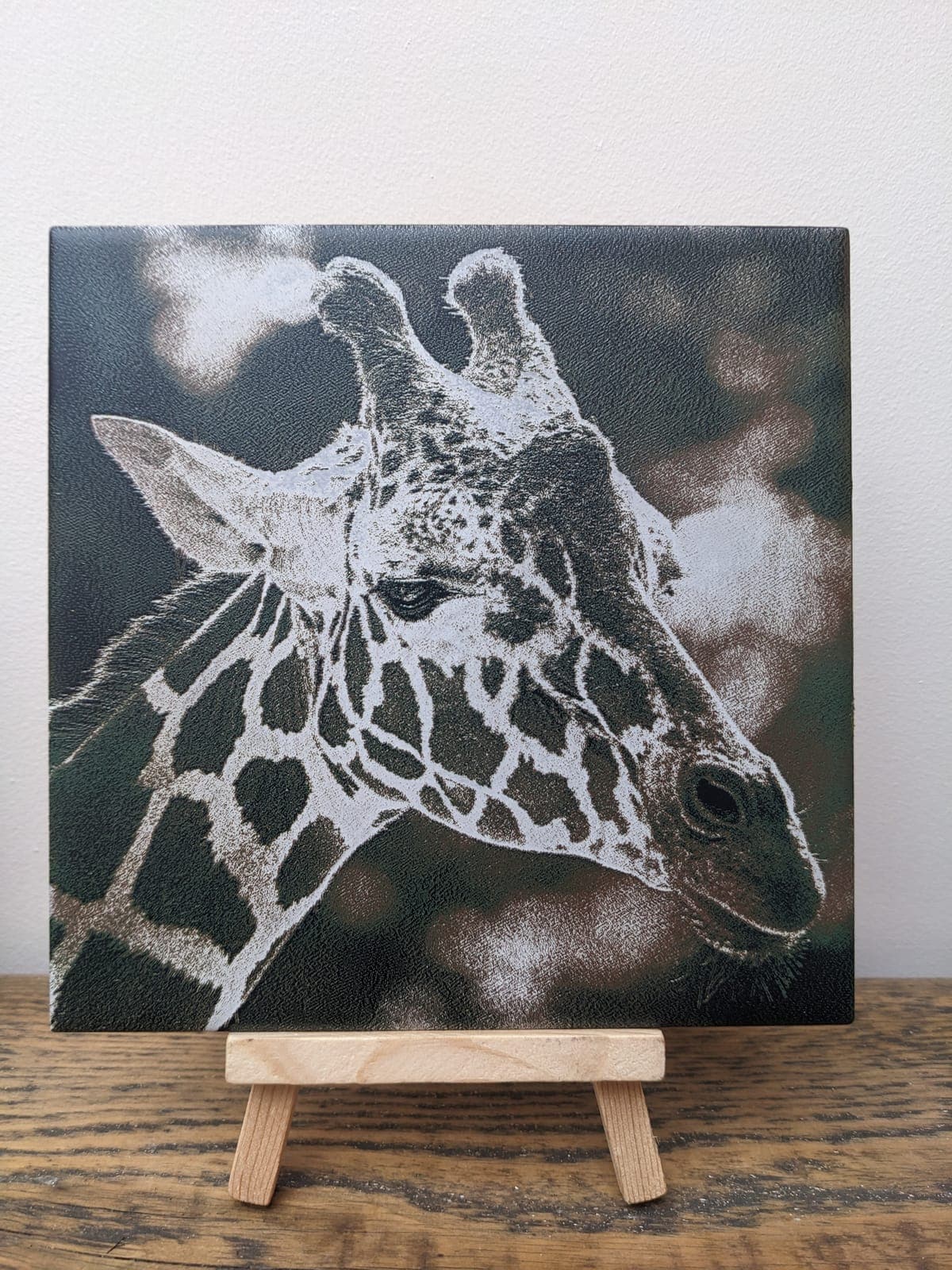 A close-up of a giraffe's head engraved on a tile, on a small easel