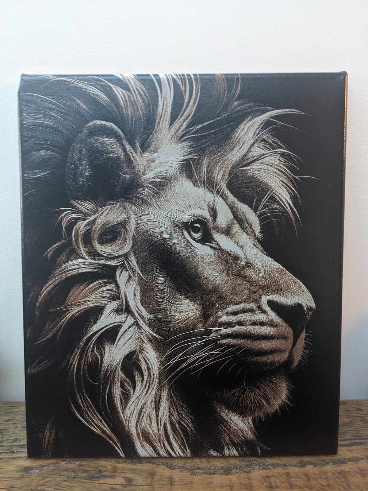 A lion's head in profile with a flowing mane, engraved on a dark tile
