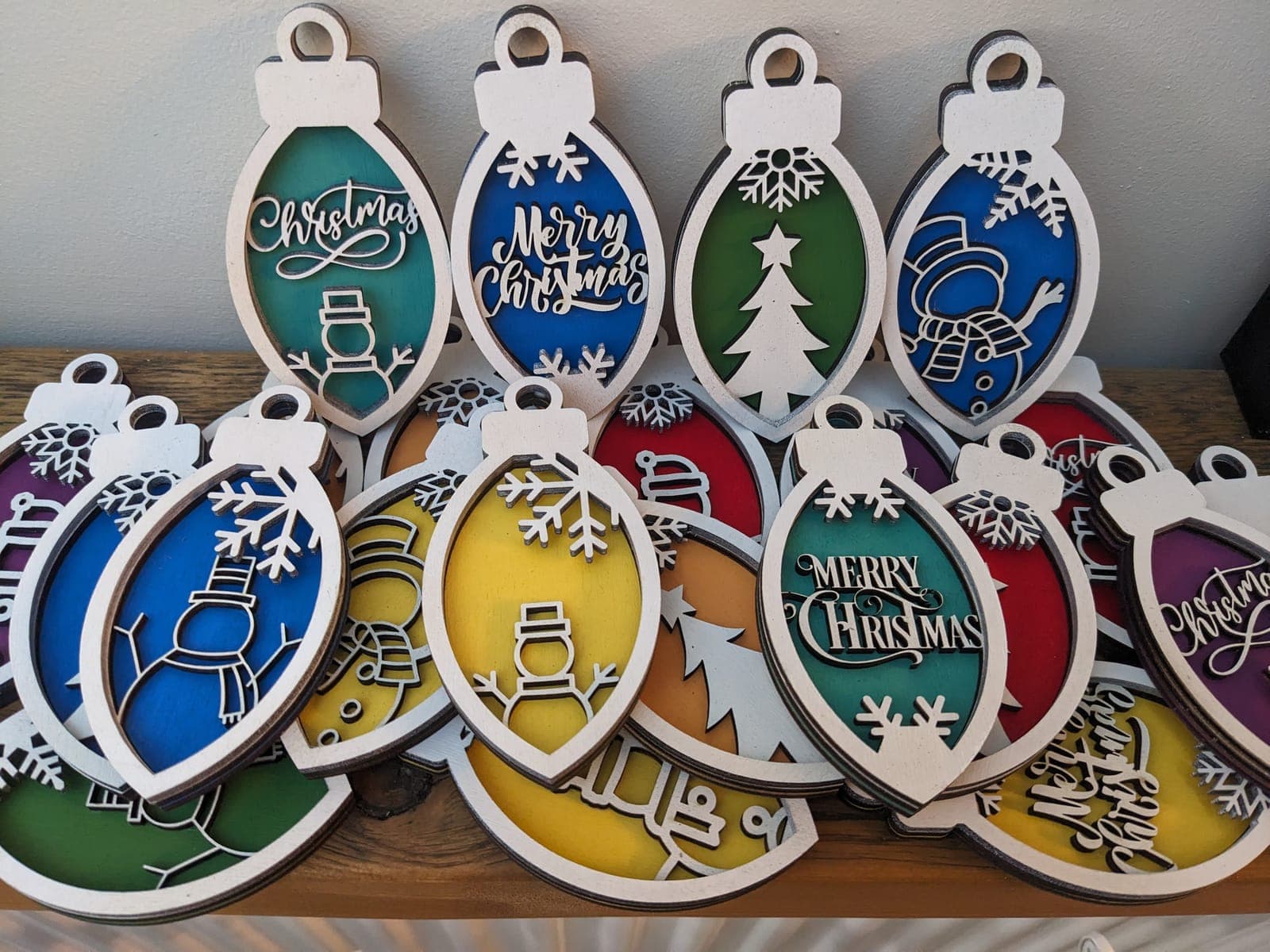 A pile of layered wooden baubles in bright colours with snowflakes, trees and Merry Christmas cut-outs